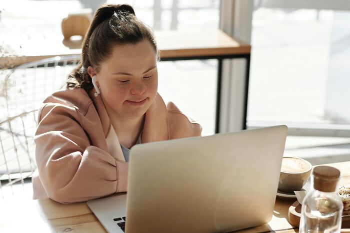 Young woman working on laptop in bright cafe, illustrating challenges of workplace rules that annoy everyone.