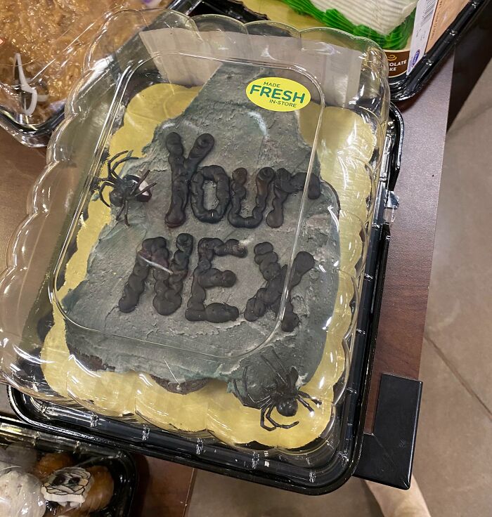 Halloween fails with misspelled "Your New" message on gray tombstone-style cake decorated with fake spiders in plastic container
