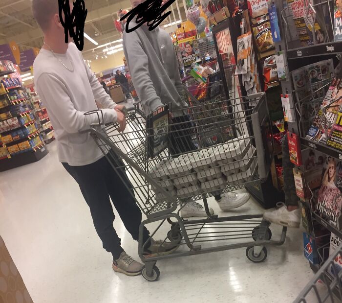 Two people pushing a shopping cart filled with eggs in a store aisle, an example of Halloween fails.