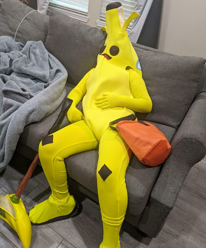Person in a banana costume slouching on a couch showing a Halloween fail with an orange trick-or-treat bag nearby.
