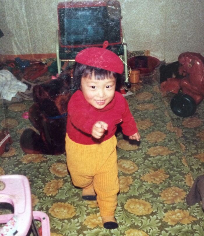 Young child wearing red and yellow outfit playing indoors on floral carpet, capturing a wild and wonderful 1980s moment.