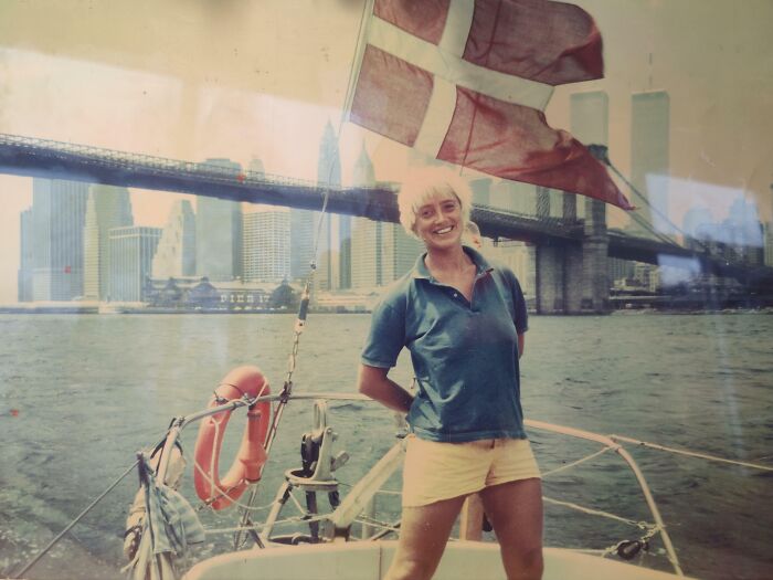Smiling woman on a sailboat wearing 1980s style clothing with city skyline and bridge in the background, 1980s photo.