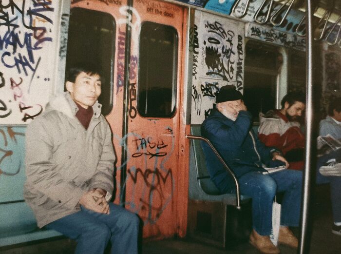 Passengers sitting inside a graffiti-covered subway car, showcasing the wild and weird 1980s urban scene.