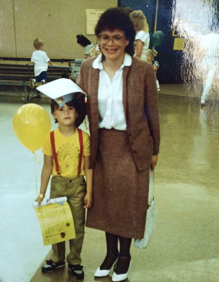 Child with yellow balloon and graduation cap stands next to smiling woman in 1980s attire, capturing wild 1980s moment.