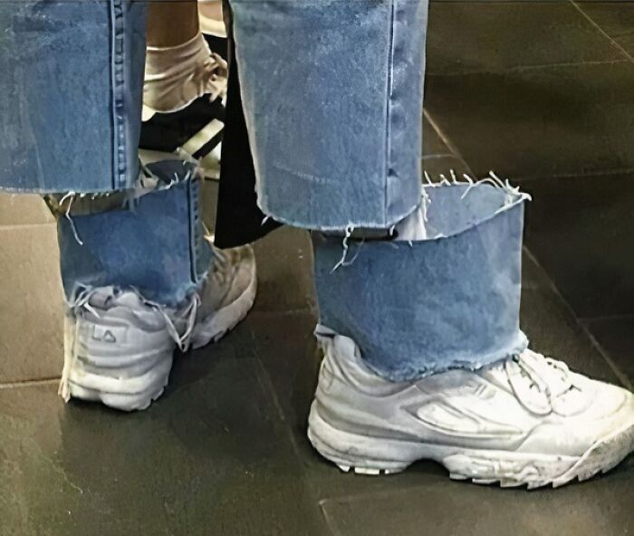 White sneakers paired with denim jeans that have unusually wide and frayed cuffs creating a confusing visual effect.
