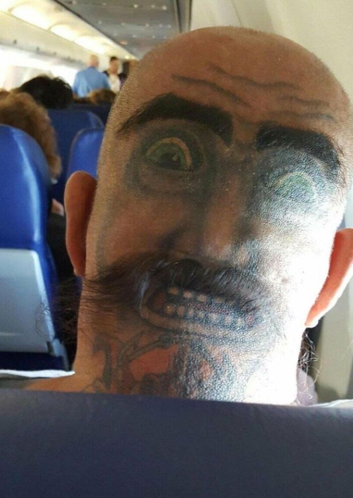 Tattoo fail of a face tattooed on the back of a bald head, creating a distorted and funny visual on an airplane seat.