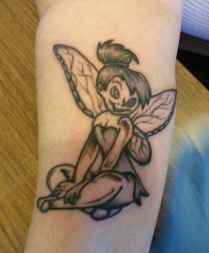 Tattoo fail of a fairy character with distorted facial features and awkward proportions on forearm.