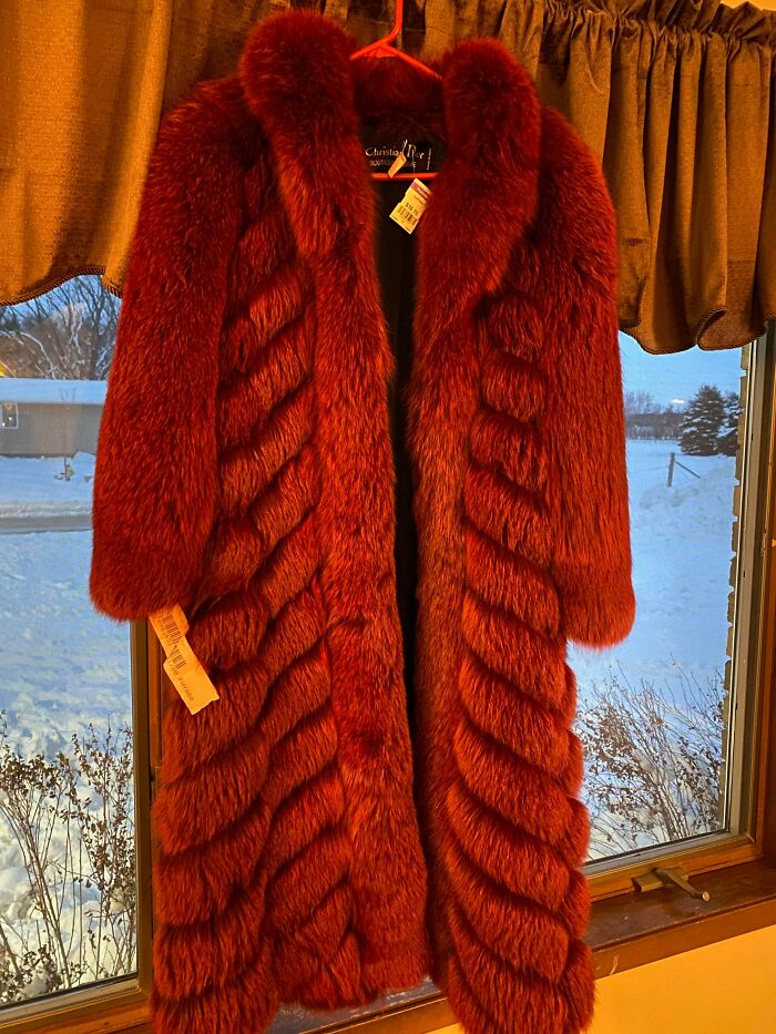 Red vintage fur coat with a price tag hanging in front of a snowy window, thrift store jackpot find.