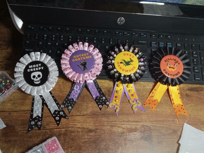 Halloween fails highlighted with decorated costume award ribbons placed on a wooden table near a laptop keyboard.