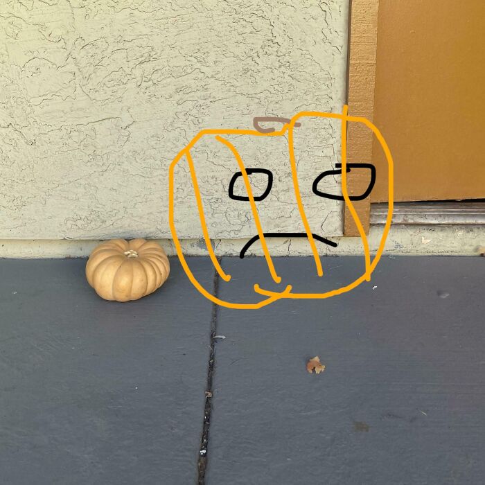A small pumpkin with a sad face drawn over it, illustrating a Halloween fail on a c*****d doorstep.