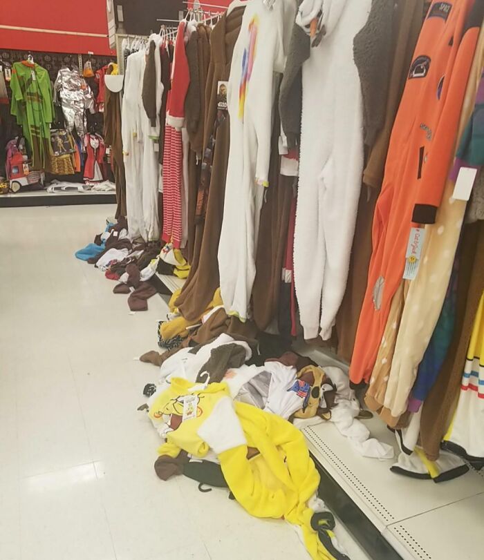 Halloween fails in a costume store aisle with outfits falling off racks and scattered mess on the floor creating a chaotic scene.