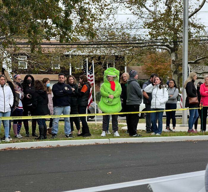 A group of people standing behind caution tape with one person in a bright green costume Halloween fails scene.