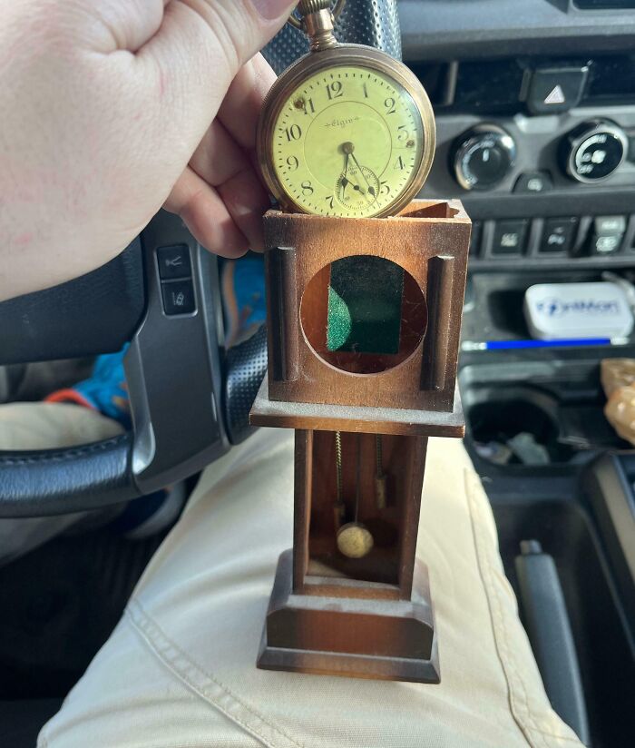 Hand holding vintage pocket watch above wooden miniature grandfather clock found by lucky thrift store shoppers.