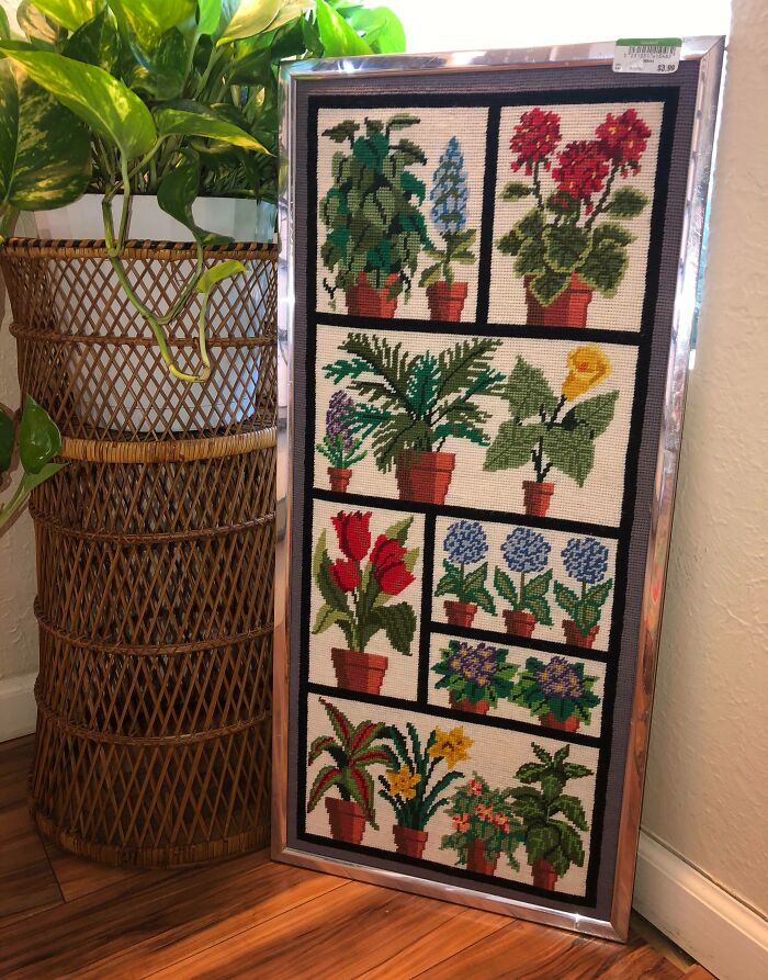 Framed vintage floral needlepoint artwork found by lucky shoppers at a thrift store displayed next to a tall plant stand.