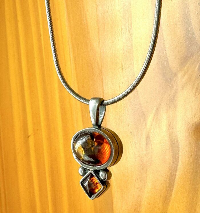 Silver pendant necklace with amber stones hanging against a wooden background, thrift store jackpot find by lucky shoppers
