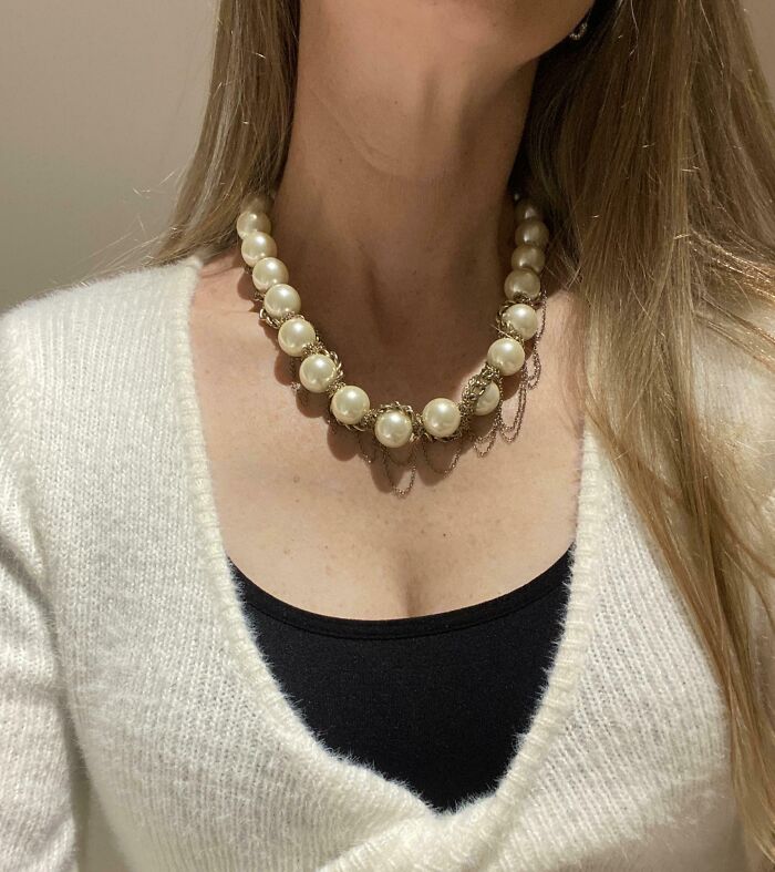 Woman wearing a vintage pearl necklace and cozy white sweater, showcasing a thrift store jackpot find.