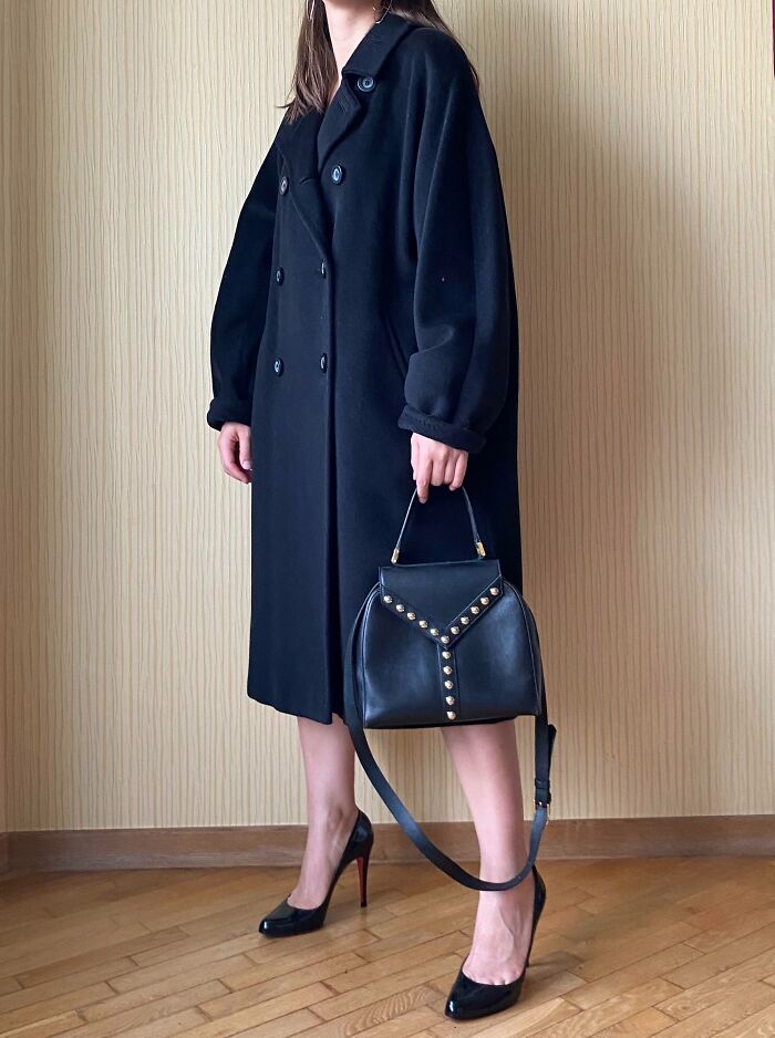 Woman wearing a black coat and heels holding a black studded handbag, showcasing a thrift store jackpot fashion find.