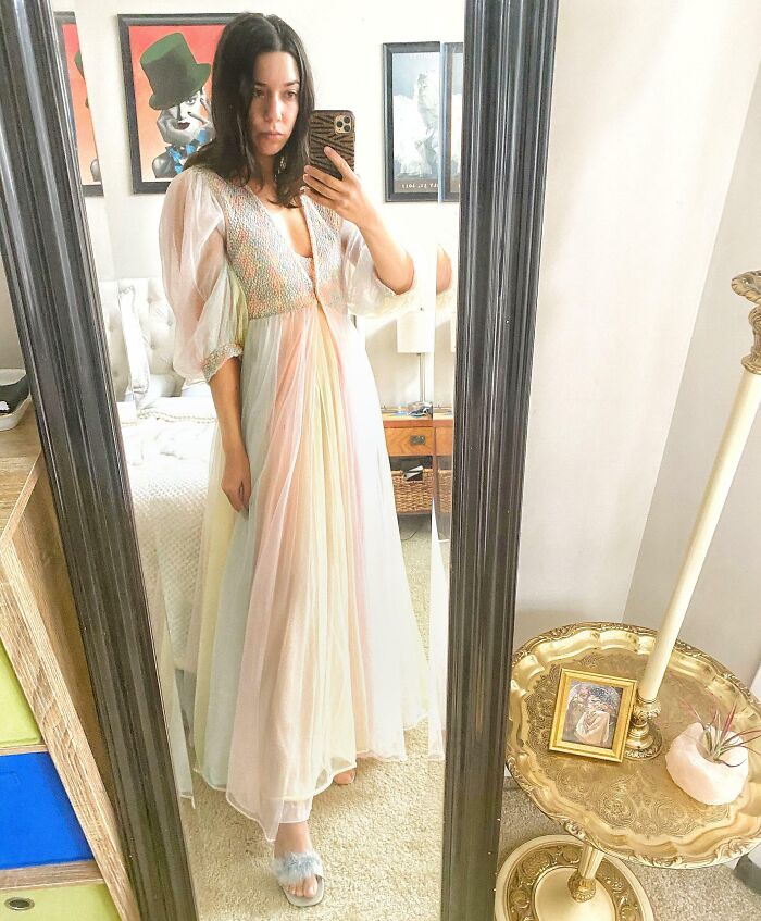 Woman in a pastel vintage dress taking a mirror selfie after hitting the thrift store jackpot with lucky finds.
