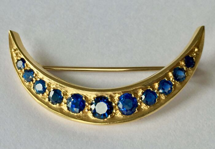 Gold crescent-shaped brooch with blue gemstones, a thrift store jackpot find by lucky shoppers.