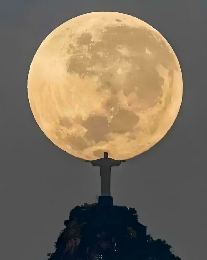Silhouette of Christ the Redeemer statue against a large, glowing full moon in the night sky, a picture that goes hard.