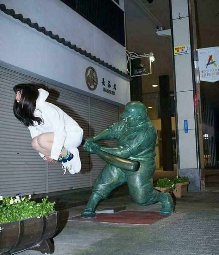 Woman jumping next to a baseball statue, creating a funny picture that people are chuckling at and going hard over.