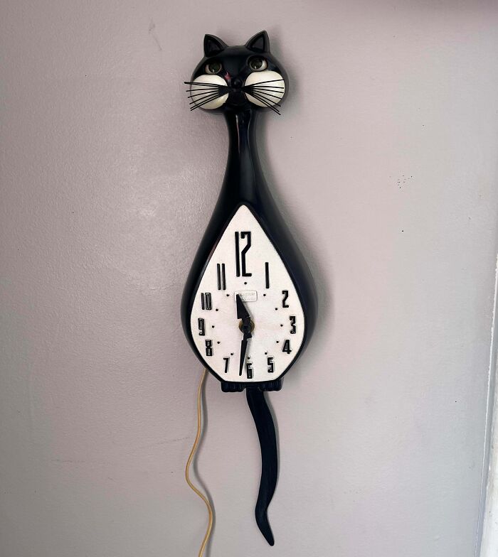 Vintage black cat wall clock found by lucky thrift store shoppers, featuring pendulum tail and retro design on a plain wall.