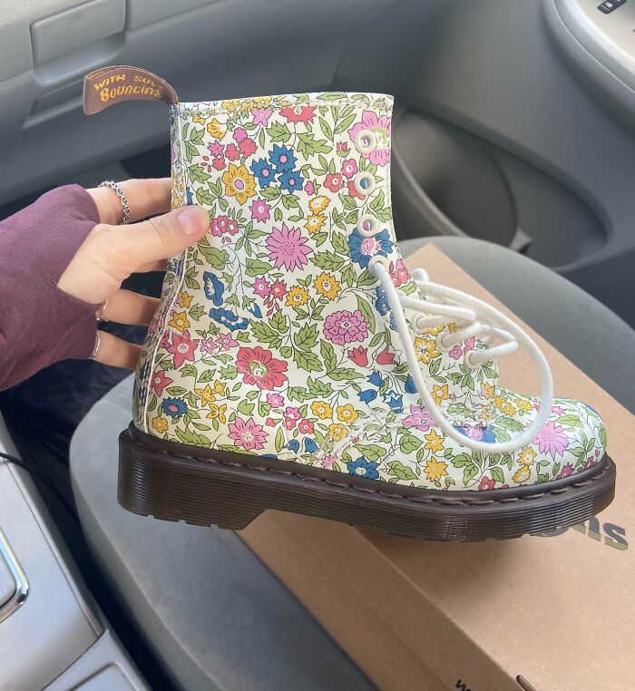 Hand holding floral print boot found thrift store jackpot, colorful pattern with white laces and dark sole inside a car.