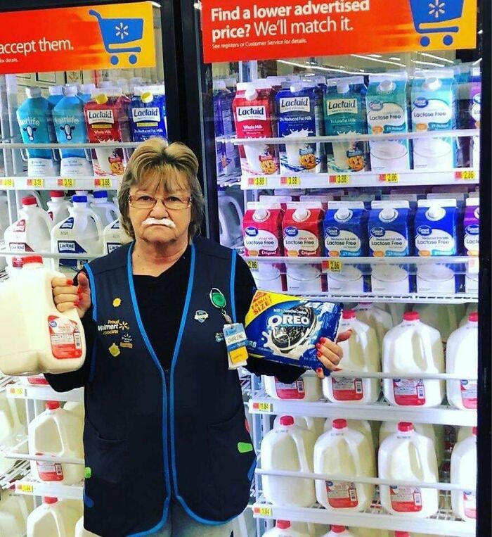 Empleado de Walmart con leche y galletas Oreo frente a refrigeradores llenos de leche en escena divertida y confusa.
