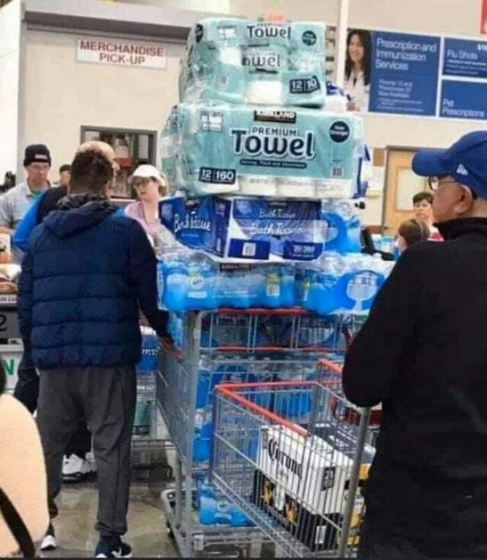 People of Walmart shopping with an overloaded cart stacked high with water bottles and paper towels inside the store.