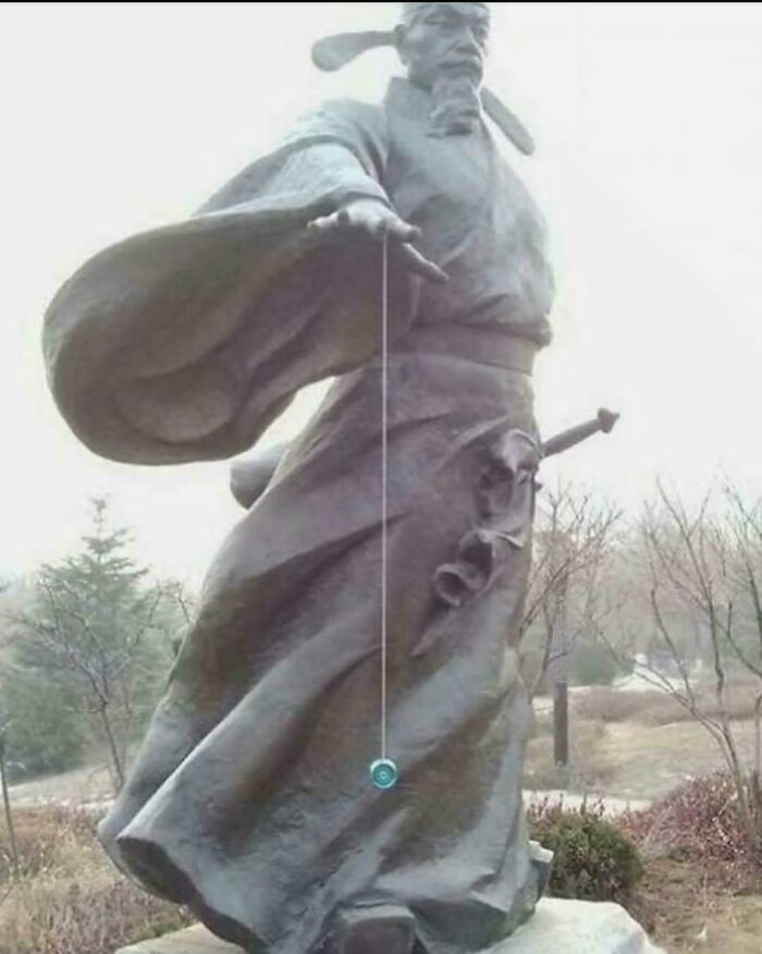 Statue of a man with outstretched arm playing with a yoyo, an unexpected funny picture that goes hard in an outdoor setting.