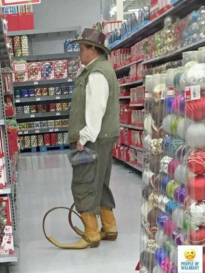 Man wearing unusual cowboy hat and oversized boots shopping in a Walmart aisle with holiday decorations.