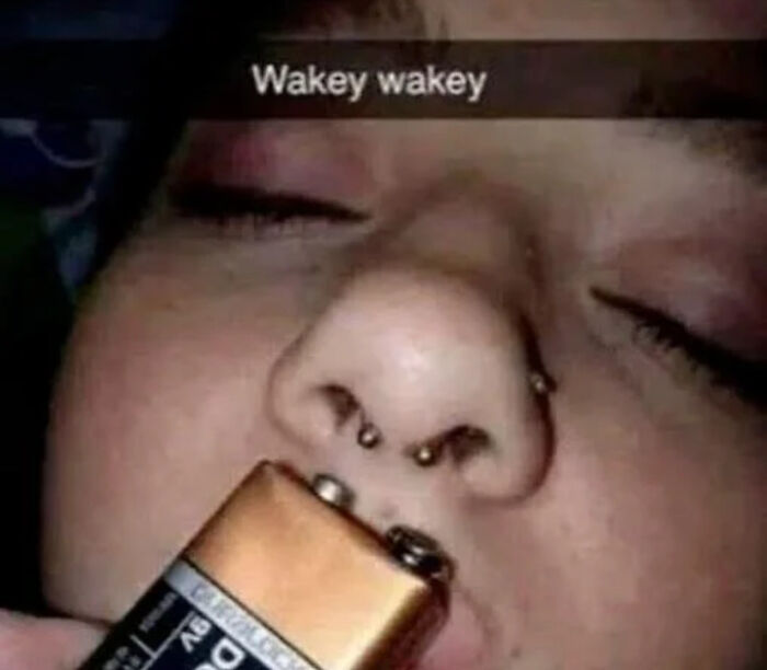 Close-up of a person with nose piercings holding a battery to their lips in a humorous picture that goes hard.