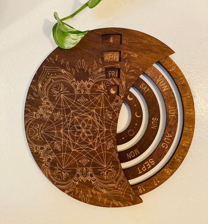 Wooden crescent-shaped perpetual calendar with engraved geometric patterns, a plant leaf, and rotating date indicators, thrift store find.