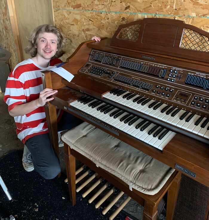 Young shopper kneeling beside a vintage organ in a thrift store, smiling after hitting a lucky thrift store jackpot.