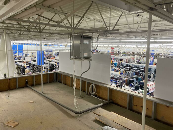 Interior view of a large Walmart store showing empty upper level and aisles filled with merchandise and shoppers below.