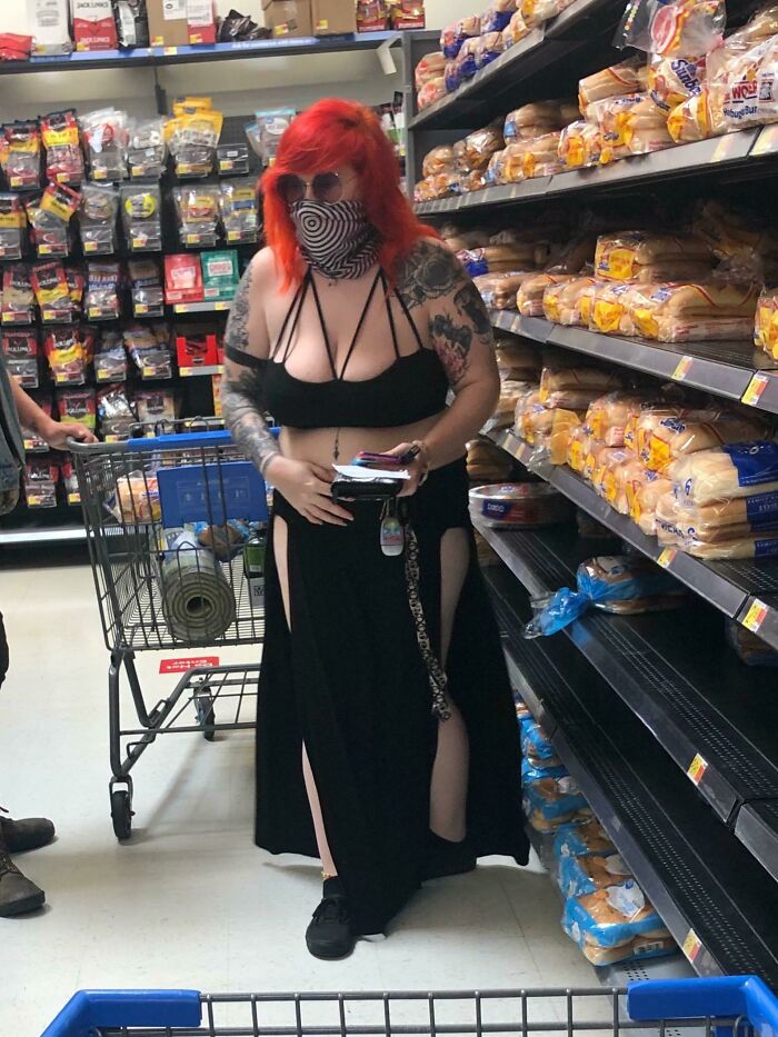 Woman with red hair and tattoos wearing a black outfit and mask shopping in a Walmart bread aisle, showcasing unique People of Walmart style.