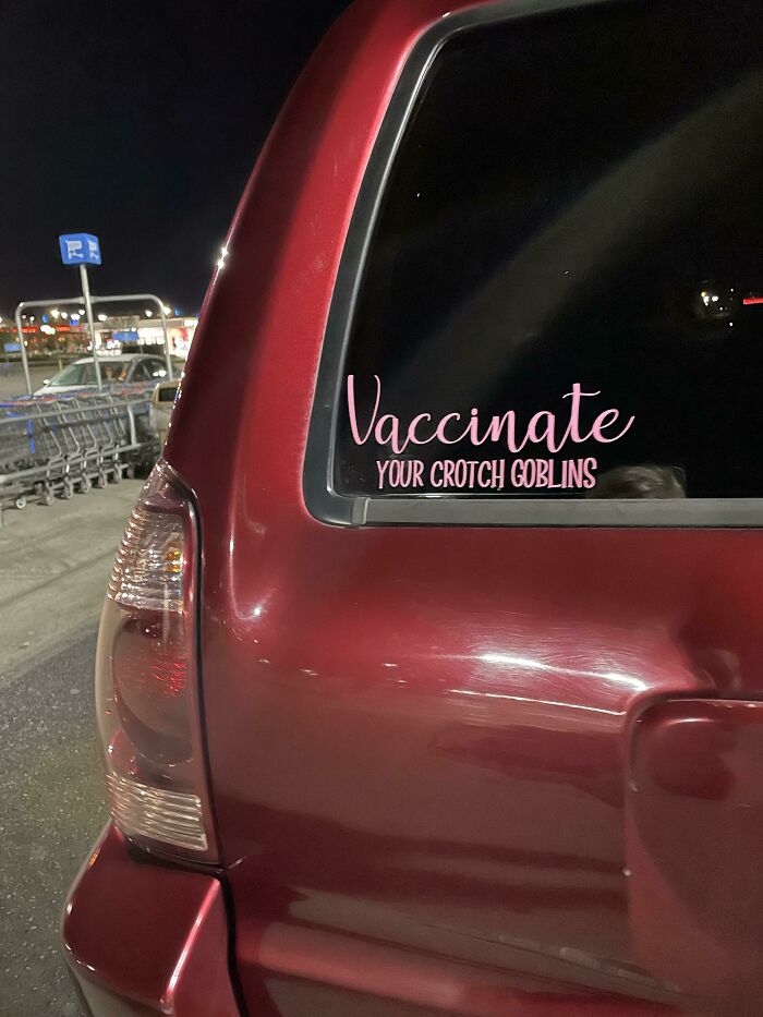 Red SUV at night with a humorous "Vaccinate your c****h goblins" sticker in a Walmart parking lot.