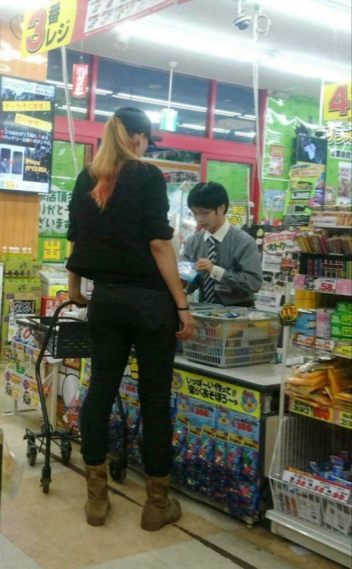 A woman with a shopping cart checking out at a busy store counter with colorful product displays around.