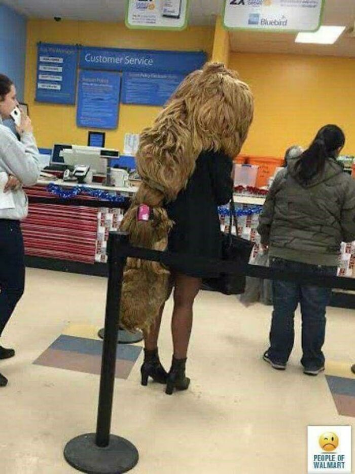 Person wearing an oversized furry coat and high heels standing in line at a customer service counter in Walmart.