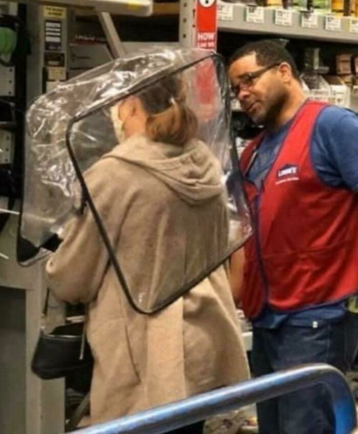 Woman wearing clear protective gear on her head shopping at Walmart with an employee assisting in a store aisle.