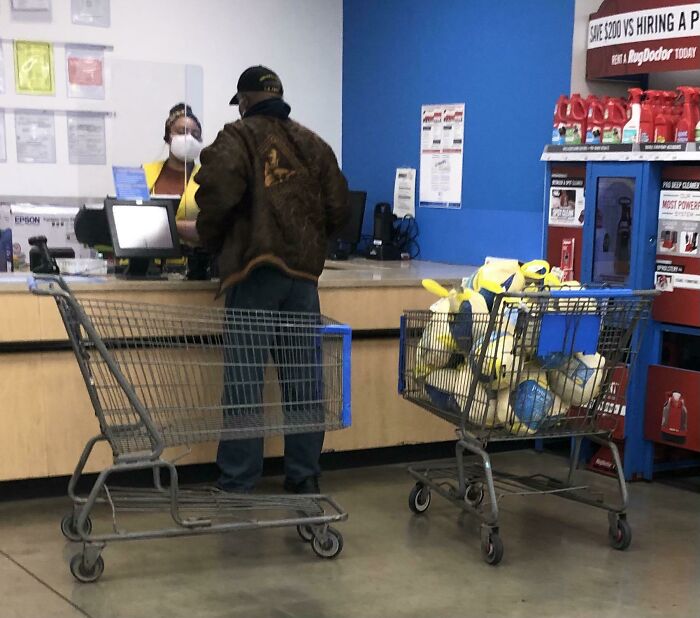 Customer wearing a jacket checking out at a Walmart register with two shopping carts, one filled with poultry products.