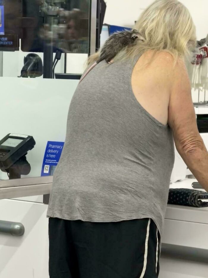 Older woman at store counter with a raccoon on her shoulder in a wild People of Walmart moment.