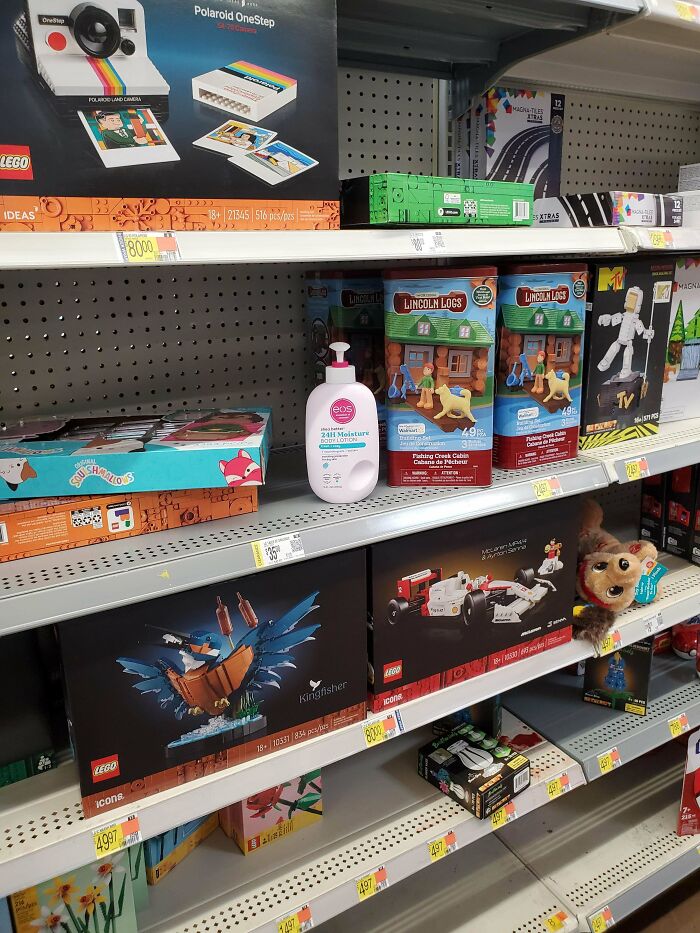 Walmart toy aisle with LEGO sets, vintage camera model, lotion bottle, and children's toys on retail shelves.