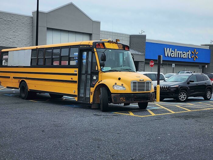 Yellow school bus parked in a Walmart parking lot with cars and store building in the background.
