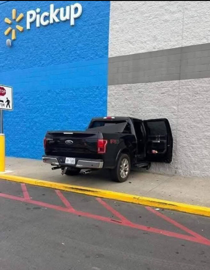 Black pickup truck parked on sidewalk near Walmart pickup area with rear door open in unusual spot.
