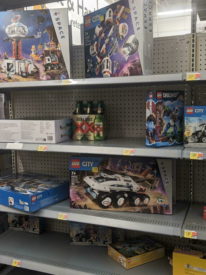 Lego City space-themed sets displayed on Walmart store shelves with some empty spots and a six-pack of Dos Equis beer.