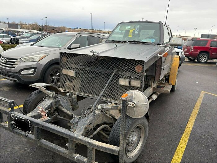 Rusty homemade vehicle with a large metal grille and exposed front chassis parked in a Walmart parking lot.