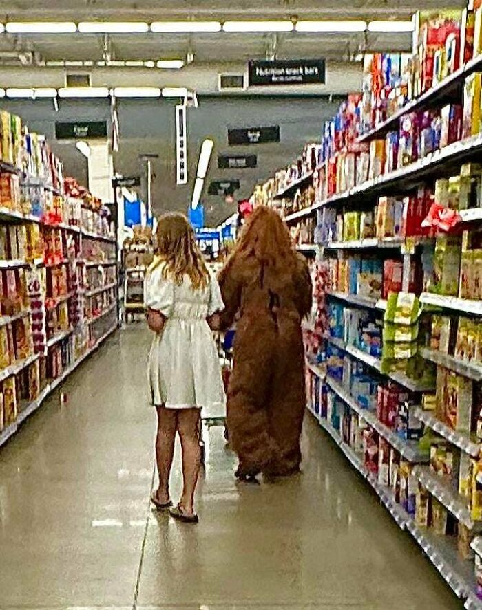 Two shoppers walking down a Walmart aisle, one wearing a white dress and the other in a full-body animal costume.