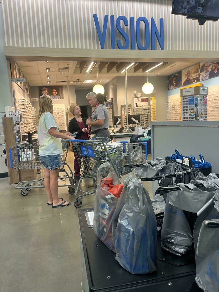 People of Walmart inside a Walmart vision center with shoppers and shopping carts near eyewear displays and checkout area.