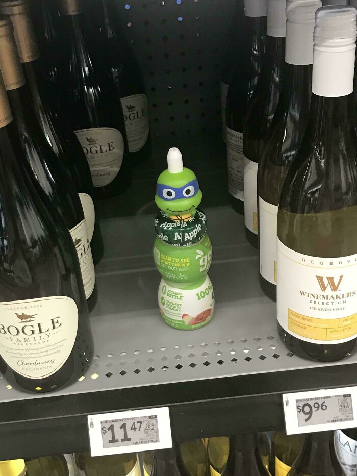 Juice bottle with a Ninja Turtle cap placed among wine bottles on a store shelf in a People of Walmart scene.